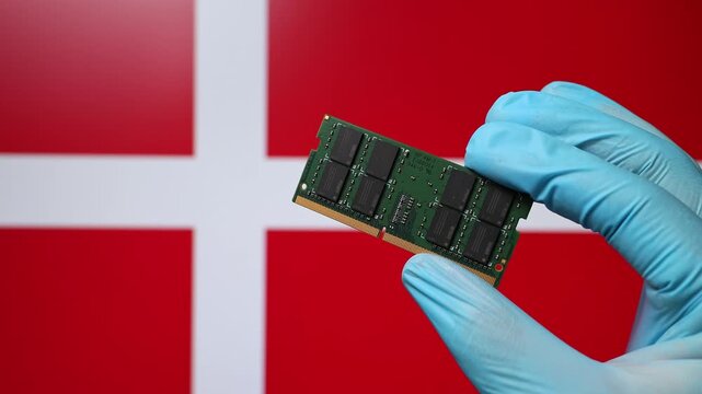 Close up view of hand in blue glove holding RAM memory microchip module. Danish flag in blurred background. Concept of semiconductor shortage, artificial intelligence development in Denmark.