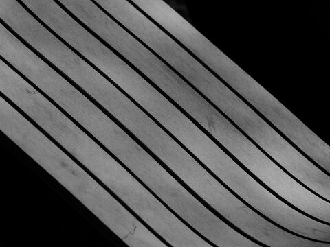 high contrast black and white photograph featuring a modern, curved surface with sharp, parallel lines that create a dynamic sense of motion against a dark background, park bench