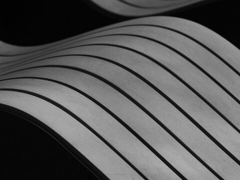 high contrast black and white photograph featuring a modern, curved surface with sharp, parallel lines that create a dynamic sense of motion against a dark background, park bench