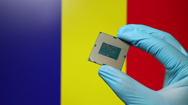 Close up view of hand in blue glove holding CPU microchip. Romanian flag in blurred background. Concept of semiconductor shortage and artificial intelligence development in Romania.