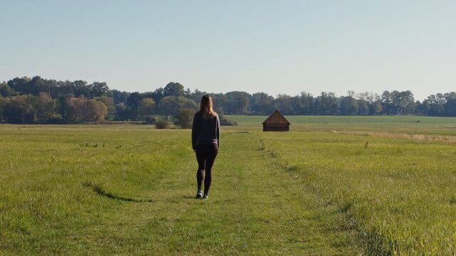Woman walking through a scenic green meadow towards a traditional historic wooden hay barn in Trebon, Czech Republic