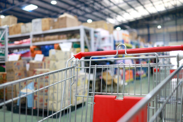 Empty shopping cart inside a large retail store, with blurred shelves and cardboard boxes in the background, shopping, wholesale, retail business and consumer lifestyle © cgdeaw