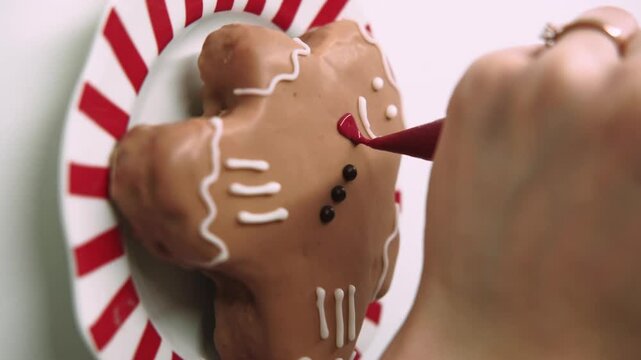 Vertical video. Decorating cookie. Confectioner work. Female hand drawing with red topping cream piping bag on sweet gingerbread man.