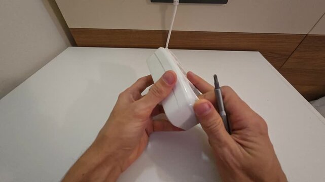 Technician repairs electric extension cord with screwdriver over desk, preventing shock hazard through cautious work. Deliberate motions secure power strip housing to maintain safety standards.