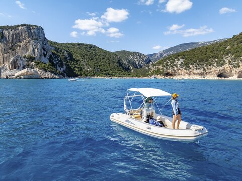 Motor boat off picturesque rocky coast, cliffs and Cala Luna beach, aerial view, Golfo di Orosei, Baunei, Sardinia, Italy