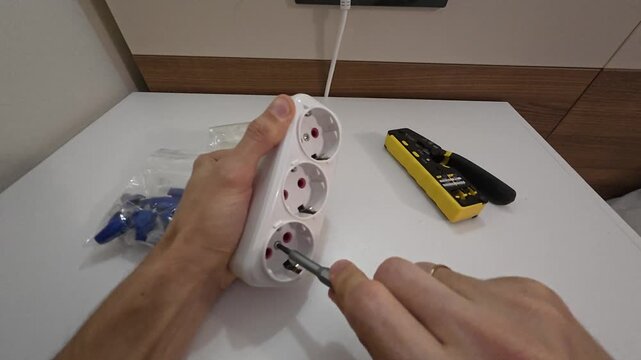 Male hands fit protective socket covers inside electrical extension board to improve child safety. Meticulous worker demonstrates essential home safety measures on modern indoor desk space.