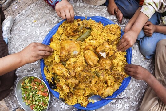 Jordan shared chicken rice platter with salad and yogurt communal dining hands eating traditional Middle East cuisine family gathering close up