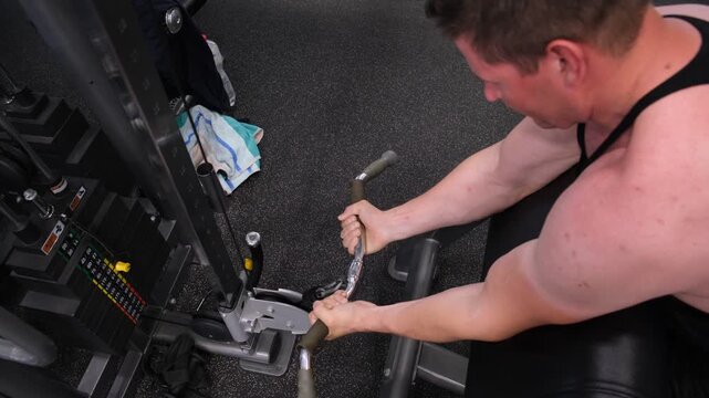 Muscular man adjusting a cable machine attachment in a modern gym, concept of strength training, workout preparation, bodybuilding, fitness routine, exercise equipment, discipline and active lifestyle