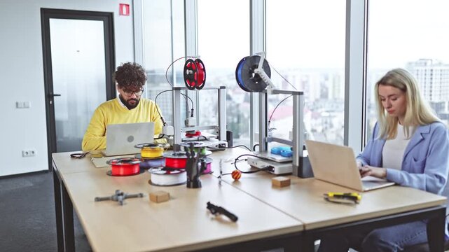 Two colleagues collaborate in a modern office space, utilizing advanced 3D printers and filament spools for rapid prototyping and design