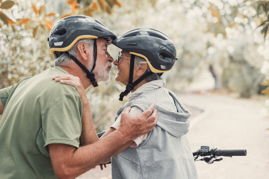 Senior couple share an affectionate embrace while cycling outdoors in a park. Elderly man and woman in helmets enjoy active retirement, love, companionship, healthy aging, and a romantic relationship.