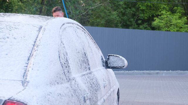 Self-service car wash station with a foam-covered vehicle being cleaned outdoors, practical footage for automotive care, maintenance, hygiene, pressure washing, consumer service, routine upkeep and ur