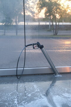 Self-service car wash bay with a pressure spray gun hanging beside a wet floor after cleaning, practical footage for washing equipment, maintenance routine, hygiene, consumer service, water use and ur