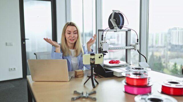 A young woman demonstrates 3D printing technology while engaging with her smartphone camera in a sleek workspace