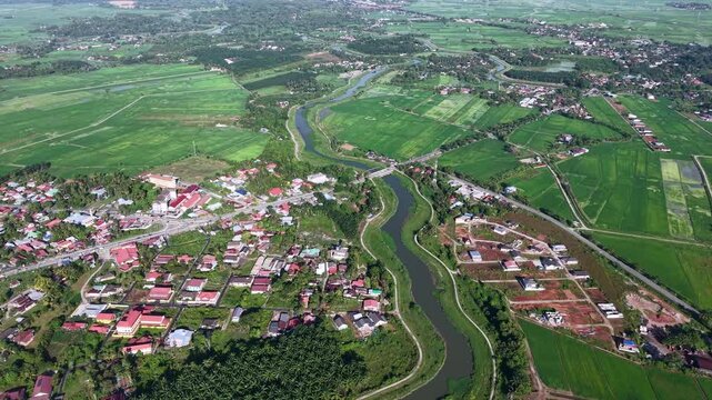 Aerial view of green fields and a meandering river. Red roofed villages dot the landscape at Kubang Semang