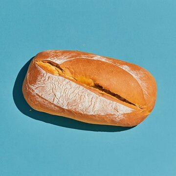 Rustic bread loaf with a floured crust on a vivid cobalt blue background, featuring a sharp shadow for bakery and food packaging layouts