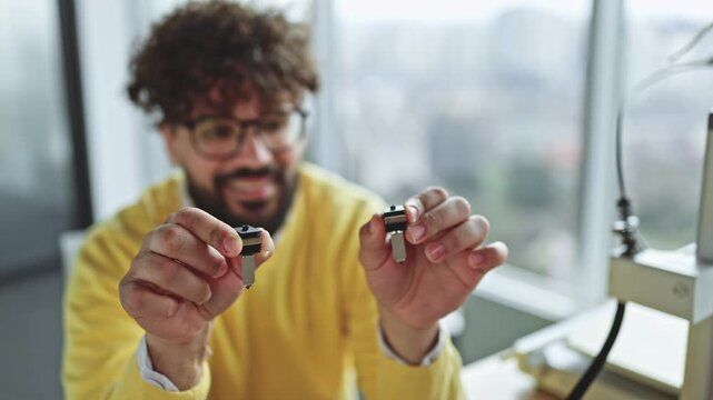 A smiling man with curly hair and glasses holds two different sized nozzles in his hands, examining them closely