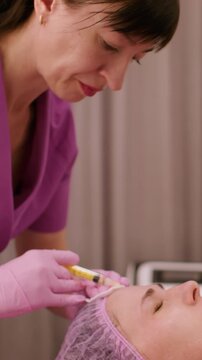 Vertical video. Beautician work. Skin care. Professional cosmetologist making botulinum toxin injection procedure for tightening wrinkles on woman face.