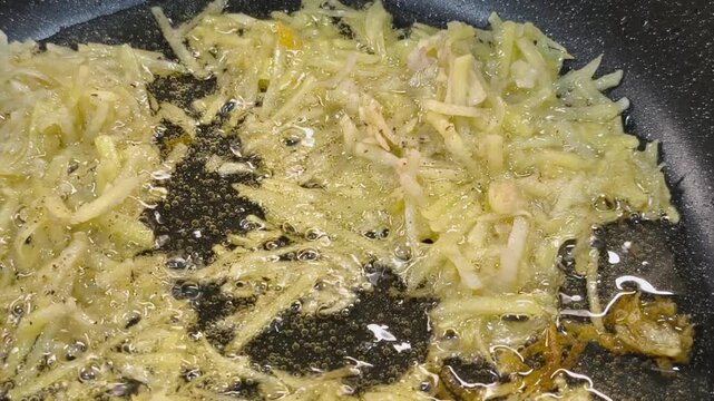 Large grated potato fritter cooking in a frying pan. Hot oil bubbles around the potato pancake as a golden crispy crust forms during frying. Homemade potato pancake made from coarsely grated potatoes.