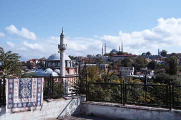Fototapeta premium Traditional patterned rug hanging on a terrace railing, with Istanbul mosques, minarets, trees and blue sky in background.