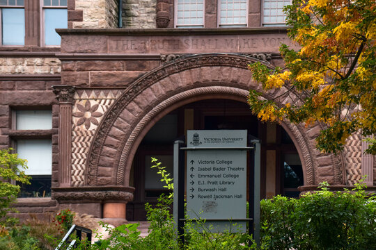 Eye-level shot of a Victoria University directional sign in front of a historic Romanesque stone archway with carved text and autumn leaves, September 2026