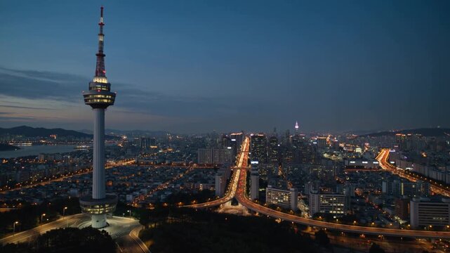 Aerial orbit around an illuminated tower above Seoul city lights at dusk