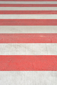 Full frame background texture of a pedestrian zebra crossing painted with alternating red and white horizontal safety lines on asphalt.