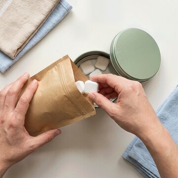 Hands Refilling Reusable Tin with Laundry Tablets