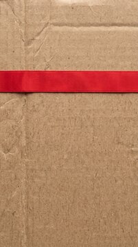 Closeup of a brown cardboard box with a red ribbon on textured surface