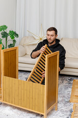 Young man assembling furniture in  living room. Concept of home improvement, © Olga Mukashev