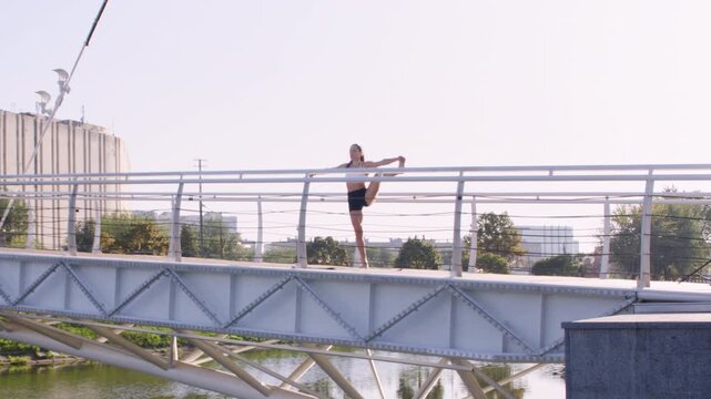Active lifestyle. City yoga. Flexible female athlete practicing sportive physical exercise performing balance pose on bridge in park.