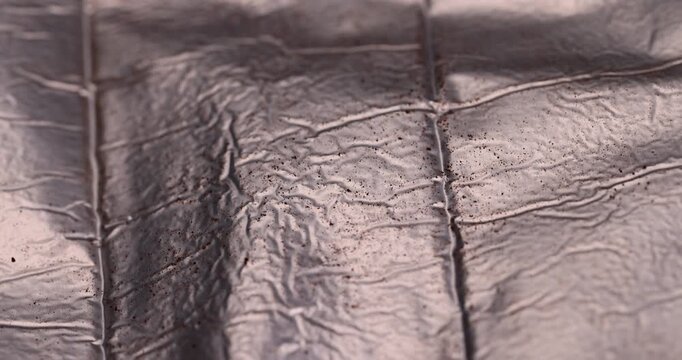 Crumpled metallic foil wrap texture background, shiny sheet surface with small dark particles on creased gold silver pattern