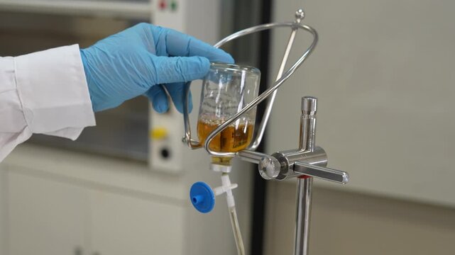 Scientist placing inverted bottle of culture medium on lab stand holder for sterility test transfer