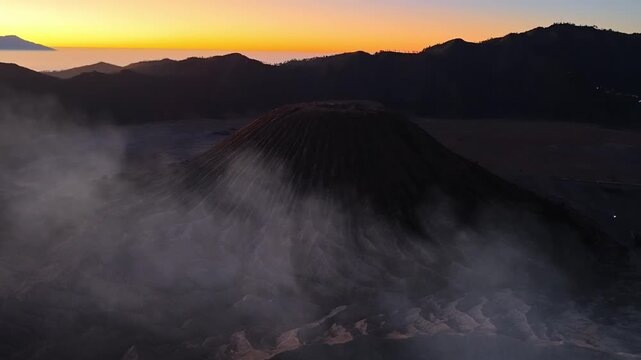 Misty volcano rises against golden dawn sky. Distant peaks fade into soft twilight hues near Bromo