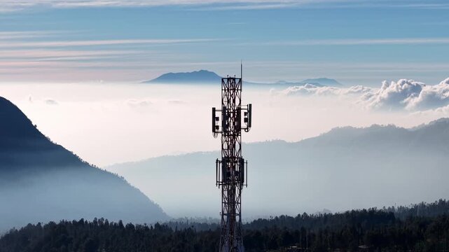 High angle view of a lonely radio mast surrounded by rolling green hills and morning mist at Cemoro Lawang highlands.