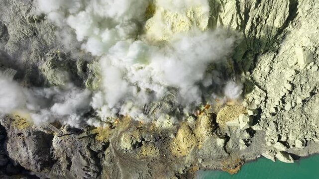 Top down aerial view of Mount Ijen crater with sulfur miners, steaming fumaroles and turquoise acid lake.