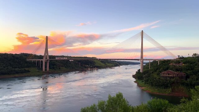 Scenic aerial footage of the Integration Bridge crossing the Parana River during a colorful sunset, connecting Brazil and Paraguay