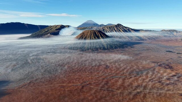 Mountains rise above misty, red earth. Vapor curls from active volcanoes at Bromo