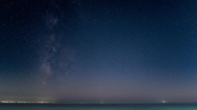 Time-lapse of Milky Way galaxy arching over limestone sea at night with moon setting and stars and distant sea horizon light