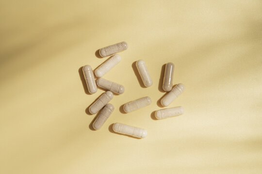 Collagen supplement capsules on yellow background with leaf shadows, flat lay and copy space