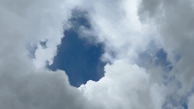 A vibrant patch of deep blue sky peaks through a dramatic frame of fluffy, light gray and white cumulus clouds.