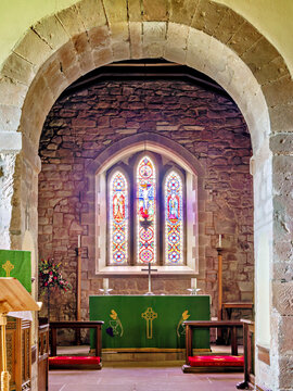 Wide view of a rounded stone arch framing a stained glass window and altar in the chancel of an old parish church
