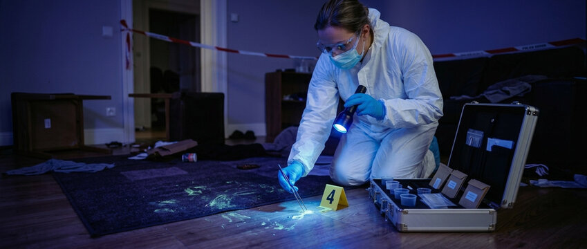 Forensic investigator examining evidence under UV light at a crime scene in a room