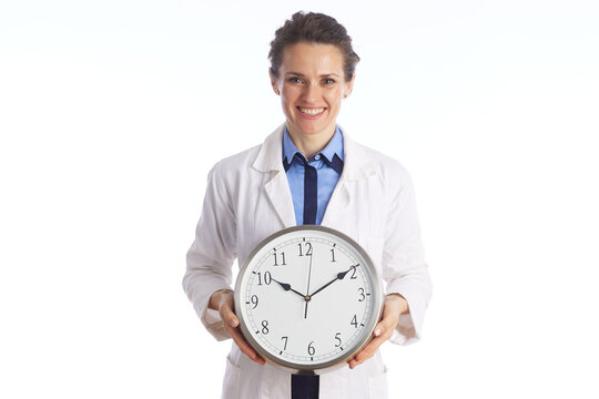 A smiling healthcare professional in a lab coat holding a wall clock, representing time management, appointment scheduling, and patient waiting times.