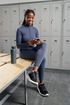 Black woman smiling using smartphone in gym locker room