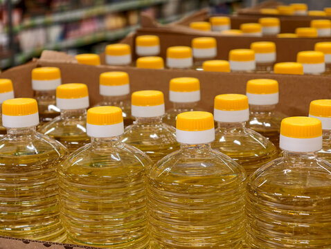 Edible sunflower oil in plastic bottles is displayed inside cardboard boxes on grocery store counters, emphasizing the packaged form and characteristic yellow color