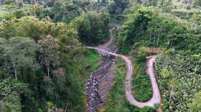 Lush green hills roll around a winding dirt path. Small wooden shack rests beside the streambed at Lumajang