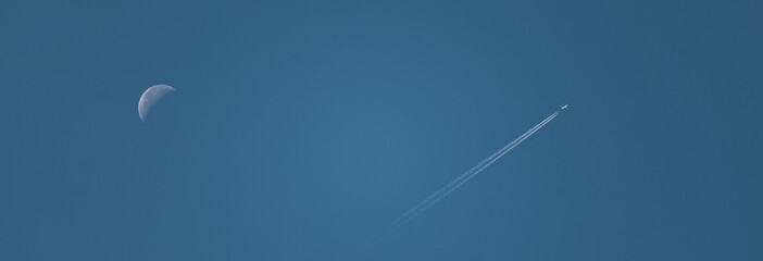 Daytime crescent moon and jet airplane with contrail in clear blue sky © Nolan