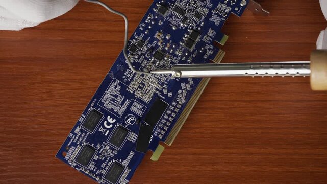 Horizontal Close Up of Soldering Iron and Solder Wire Repairing Blue Computer Circuit Board
