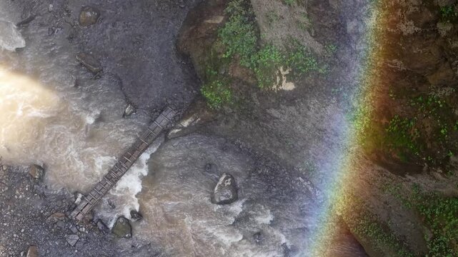 Top down drone shot of Tumpak Sewu waterfall, river canyon, rainbow mist and wooden bridge.