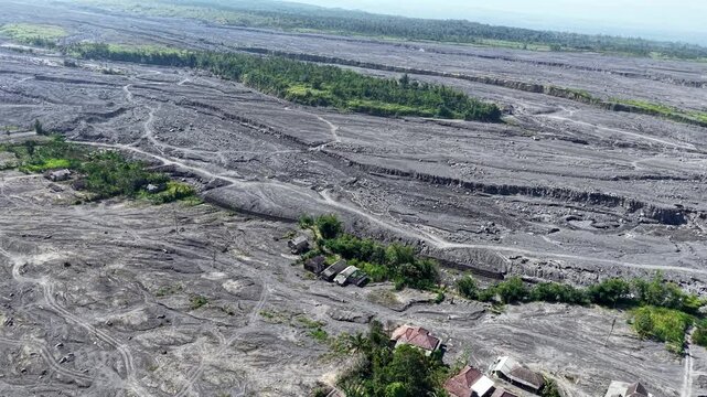 High angle drone shot overlooking a network of dry, solidified volcanic sediment channels slicing through a recovering rural countryside.